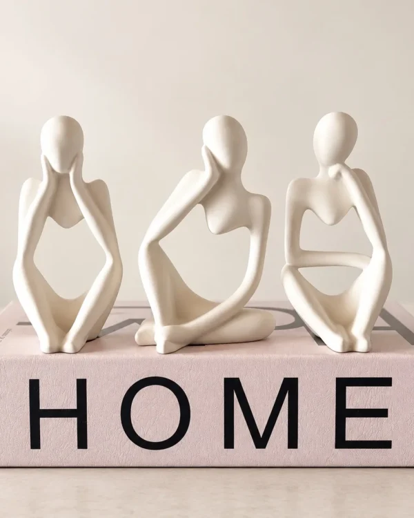 Três figuras em gesso branco sentadas sobre um livro rosa