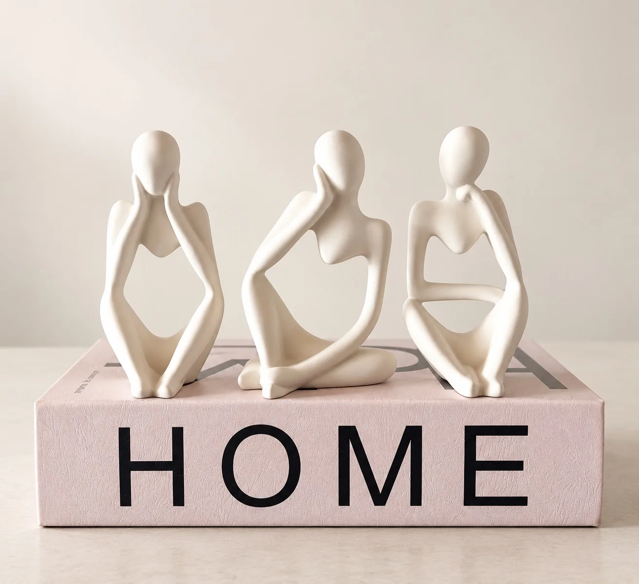 Três figuras em gesso branco sentadas sobre um livro rosa