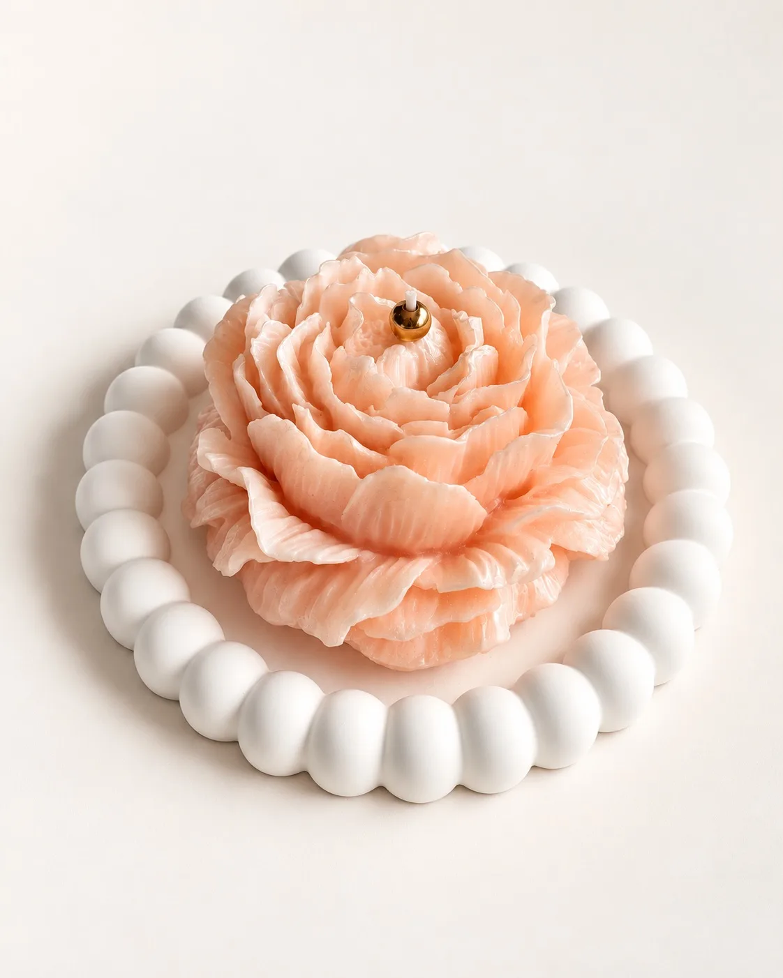 Vela em forma de peónia cor de pêssego sobre prato de gesso branco